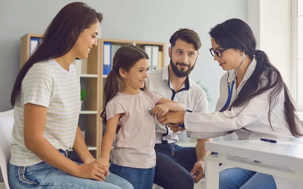 Pai, mãe e filha pequena em consulta com uma médica que examina a menina com estetoscópio