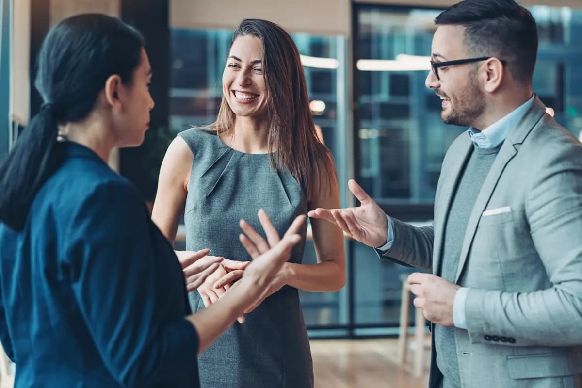Três pessoas conversam e sorriem em um escritório